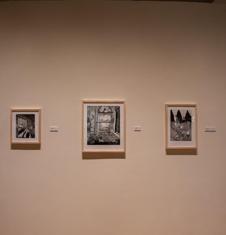 A gallery wall displays five framed black-and-white artworks of varying sizes, evenly spaced with title labels beneath each piece in a clean, minimalist exhibition space.